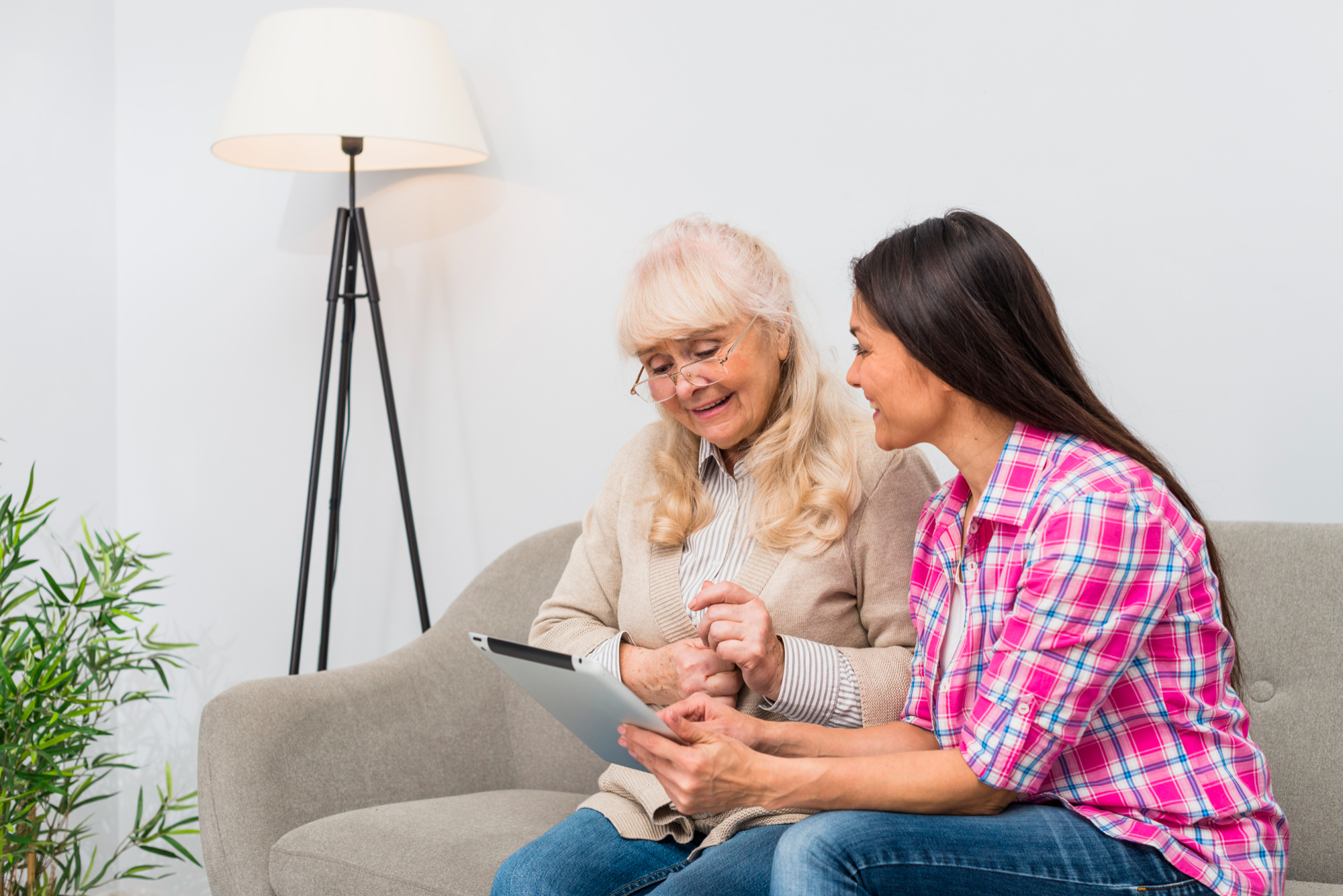 Senior woman receiving tablet guidance from a tech instructor at home.